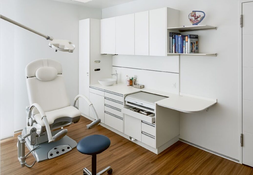 Smiling female radiographer seen through a CT scan machine gantry as she prepares a patient for a medical exam, highlighting friendly patient care and advanced medical technology.